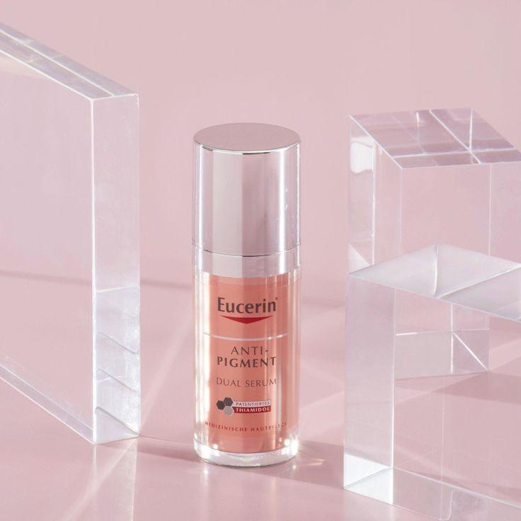 Eucerin Anti-Pigment Dual Serum in einem eleganten Flakon mit silbernem Deckel, präsentiert auf einem rosa Hintergrund mit transparenten Acrylblöcken. Wirksames Serum zur Reduzierung von Pigmentflecken und für einen strahlenden Teint.
