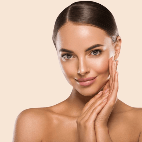 Junge Frau mit glatter, strahlender Haut und zurückgebundenem Haar hält ihr Gesicht sanft in den Händen. Symbol für Anti-Aging und Hautpflege.