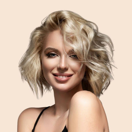 Porträt einer lächelnden Frau mit welligem, blondem Haar vor einem beigefarbenen Hintergrund.