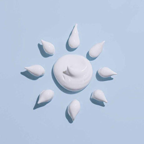 "Kreatives Muster aus Sonnencreme-Tropfen auf einem pastellblauen Hintergrund, arrangiert in einer Sonnenform, symbolisiert Schutz und Pflege unter der Sonne.