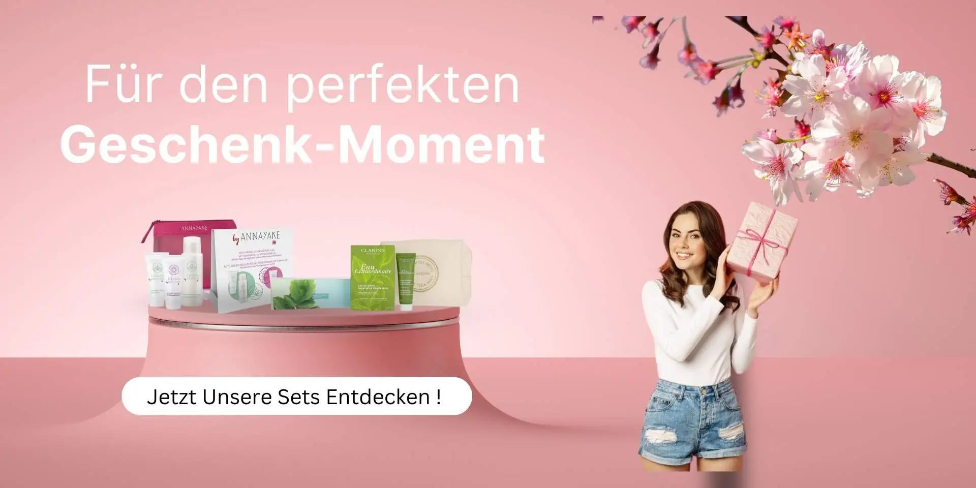 Werbebanner von parfümreich mit dem Slogan ‚Für den perfekten Geschenk-Moment‘ – links Pflege-Sets auf einem Präsentationstisch, rechts eine lächelnde Frau mit Geschenkbox vor rosa Hintergrund mit Kirschblüten.